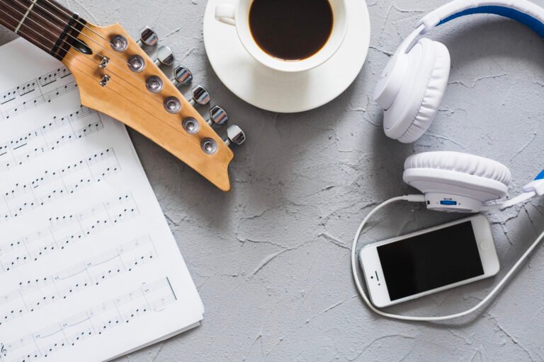 sale un conjunto de un instrumento, una taza, un movil, aurixulares y una libreta sobre aspectos del sector musical